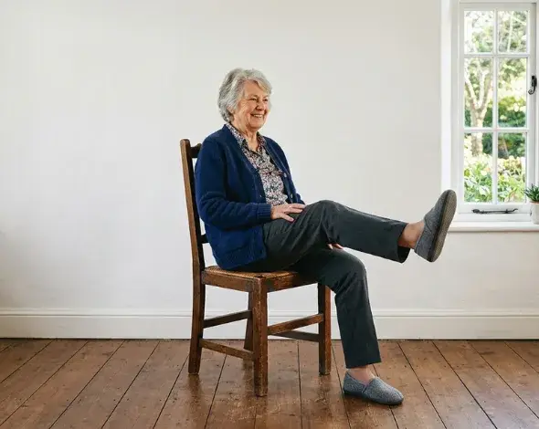 Elderly woman sitting on a chair, raising one of her legs.